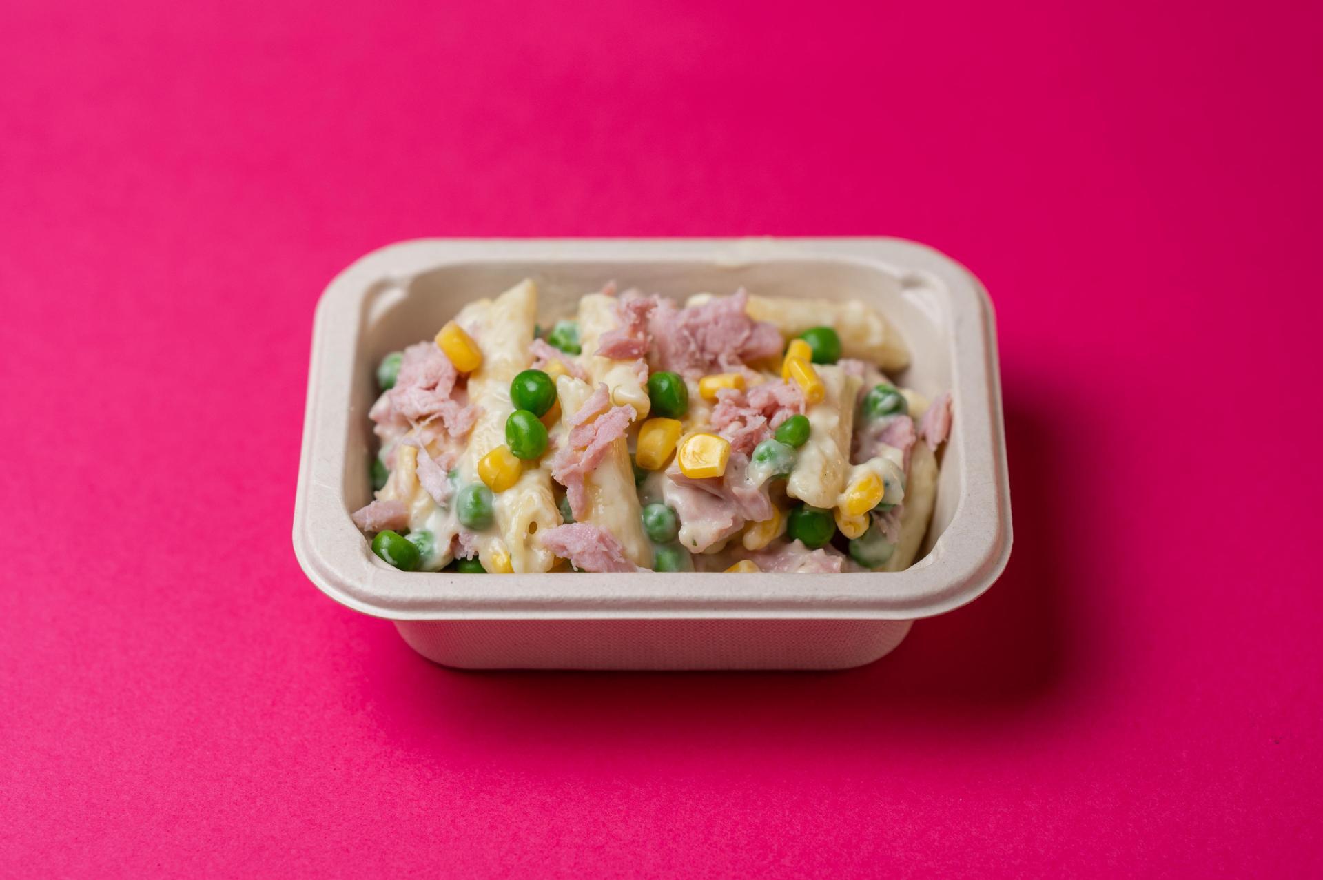 carbonara dish on a pink background with peas and sweetcorn